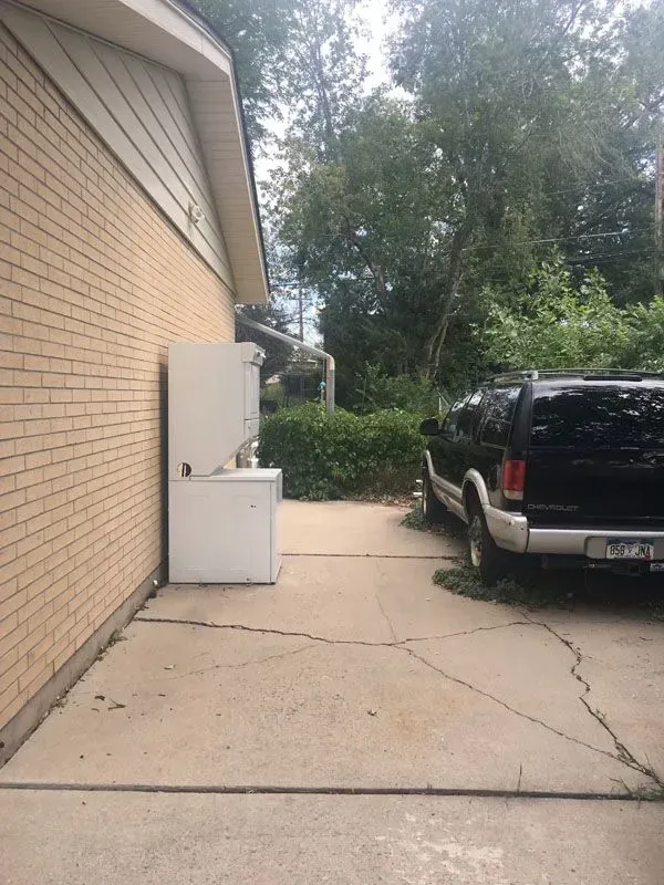 Side of a house with stacked white washer and dryer, concrete driveway, and black SUV.