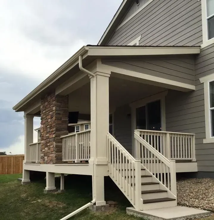 Beige and stone covered porch with stairs, railing, and guttering, attached to a house.