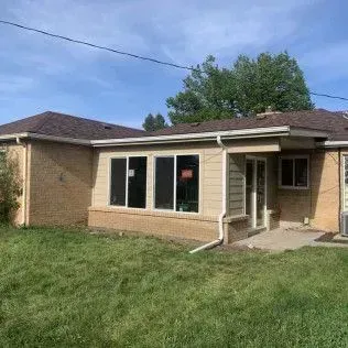 Backyard view of a beige and brown brick house with large windows, set on a green lawn.