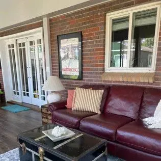 Red leather sofa in a brick-walled sunroom with a framed poster, trunk coffee table, and French doors.
