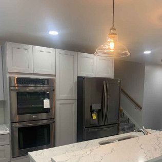 Kitchen with light gray cabinets, stainless steel double oven, black refrigerator, and glass pendant light.