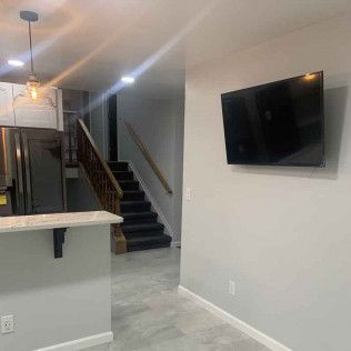 Interior of a home with a TV on the wall, kitchen area, and a staircase leading upstairs.