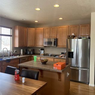 A kitchen with light brown cabinets, stainless steel appliances, and an island with a brown countertop.