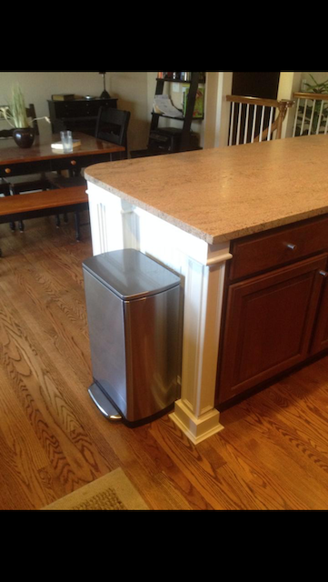 Kitchen island with a brown countertop, white trim, and a stainless steel trash can.