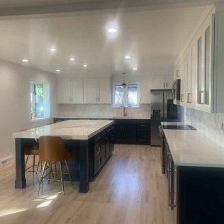 Modern kitchen with white and dark blue cabinets, light wood floors, island with stools.