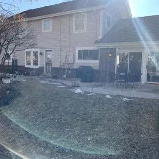 Backyard of a two-story house with grass, a patio, and sliding glass doors.