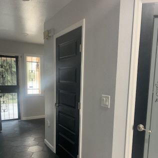 Hallway with black door, grey walls, and black hexagonal floor tiles.