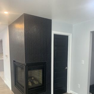 Black tiled fireplace with a black door to the right. White walls, a doorway to the left.