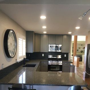 Gray kitchen with granite countertops, stainless steel appliances, and a large clock.