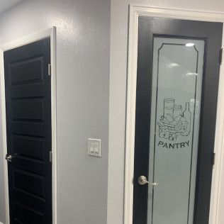 Two interior doors: one black, solid; the other a frosted glass pantry door with black trim and a pantry decal.