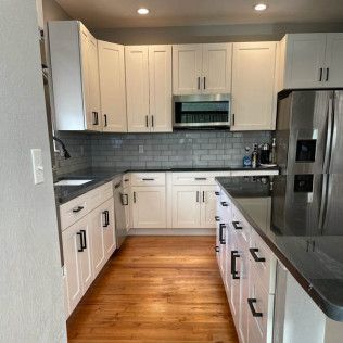 White kitchen with dark countertops and wood floors. Stainless steel appliances and white cabinetry.