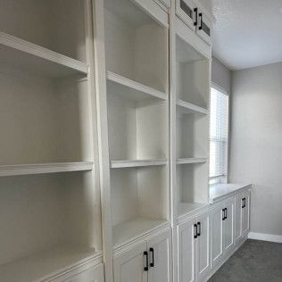 White built-in bookshelves with lower cabinets in a room, with a window and gray walls.