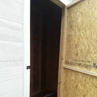 Open wooden shed doorway with white siding and exposed particleboard.