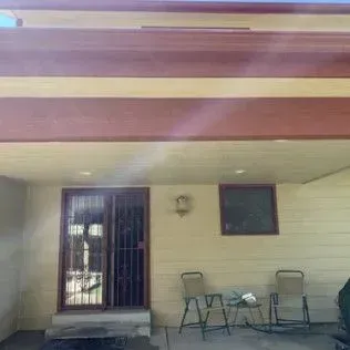 Covered patio with sliding glass door and chairs. Brown and beige exterior with a small window.