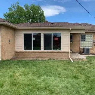 Exterior of a beige house with three large windows. Green grass in front, blue sky in background.