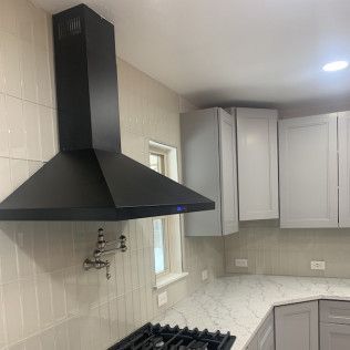 Black range hood over a stove in a kitchen with white cabinets and counter.
