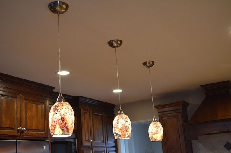 Three pendant lights hanging above a kitchen counter, with dark brown cabinets.