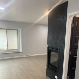 Modern living room with fireplace, gray walls, wood flooring, window, and black fireplace facade.