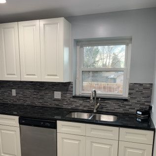 White kitchen cabinets with black countertops and mosaic tile backsplash; window over the sink.