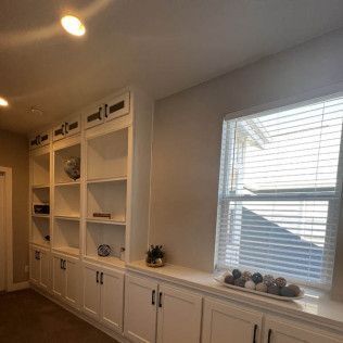 Built-in white bookshelves with cabinets, window with blinds.