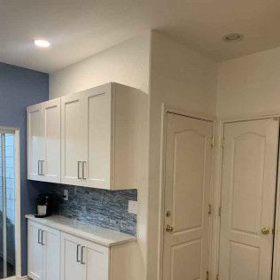 White kitchen cabinets with blue backsplash, white doors, and a coffee maker.