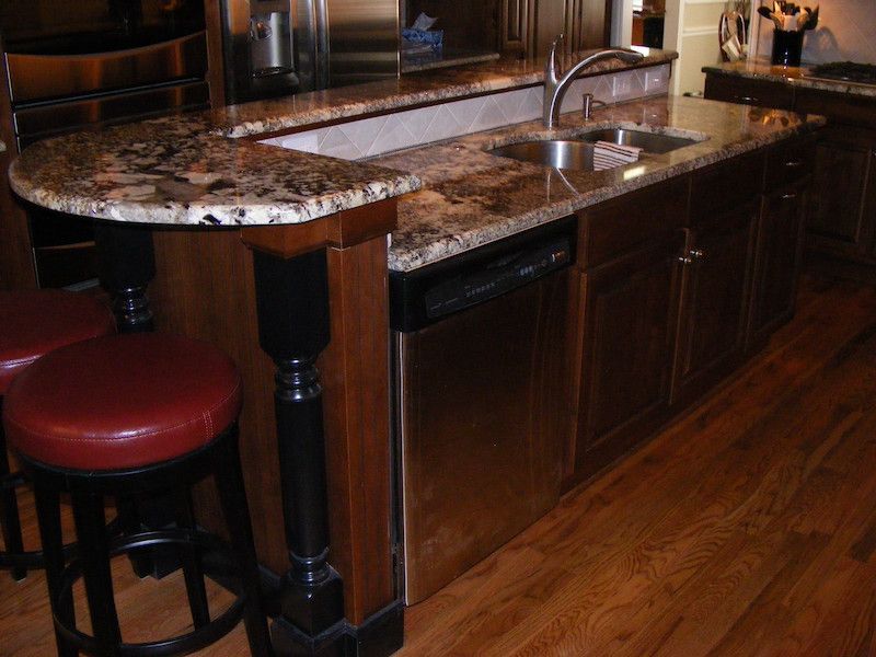 Kitchen island with granite countertop, stainless steel appliances, dark wood cabinets, and bar stools.