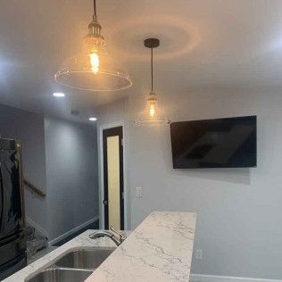 Kitchen with hanging lights over a sink, countertop, black door, and a mounted TV.