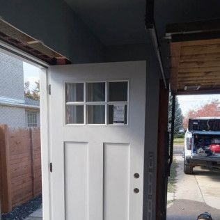 White front door with glass window panels, open in a garage, with a truck parked in the background.