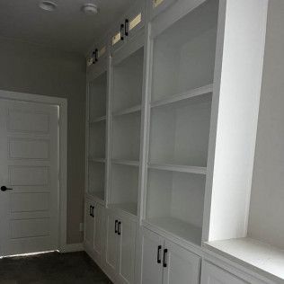 White built-in bookshelves with lower cabinets in a hallway. A white door is to the left.