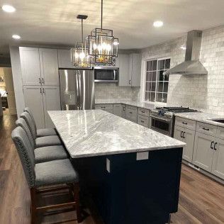 Modern kitchen with gray cabinets, marble countertops, blue island, and pendant lights.