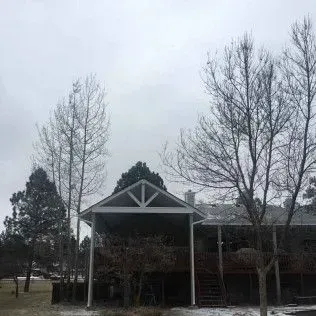 A house with a covered porch under a cloudy sky, with bare trees in the foreground.