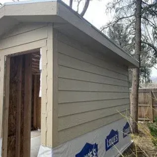 Beige shed with open doorway and horizontal siding. Lowe's logo visible on the base.