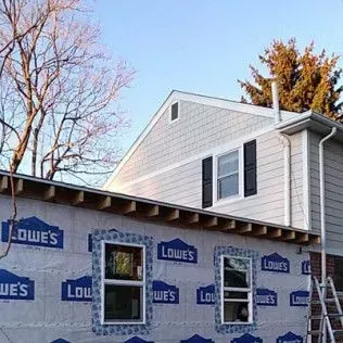 House exterior under construction, covered in Lowe's wrap. Features windows, roof, siding, and a ladder.