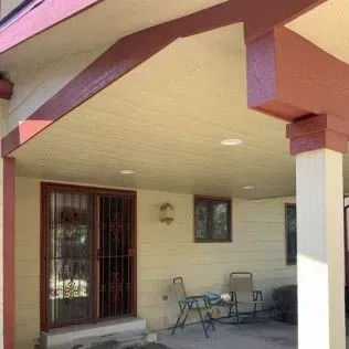 Covered patio with cream walls, burgundy trim, and a sliding door. Two chairs sit on the patio.
