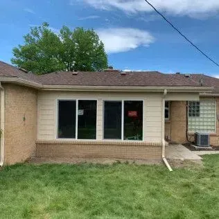 Rear view of a beige house with three large windows and a small yard.
