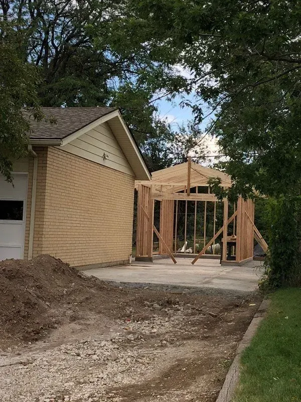 Construction of a new wooden structure next to an existing brick building with a garage door.