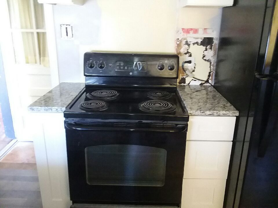 Black electric stove with four burners, granite countertops, and white cabinets.