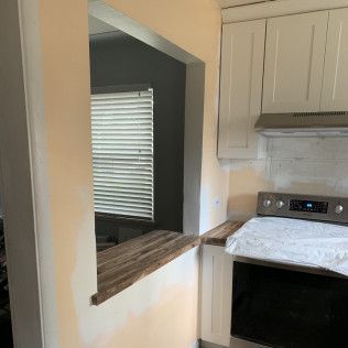 Kitchen with opening to another room, off-white cabinets, stainless steel range, and window with blinds.