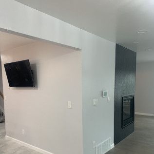 Interior view of a living space. A wall-mounted TV, a dark fireplace, and gray and white walls are visible.