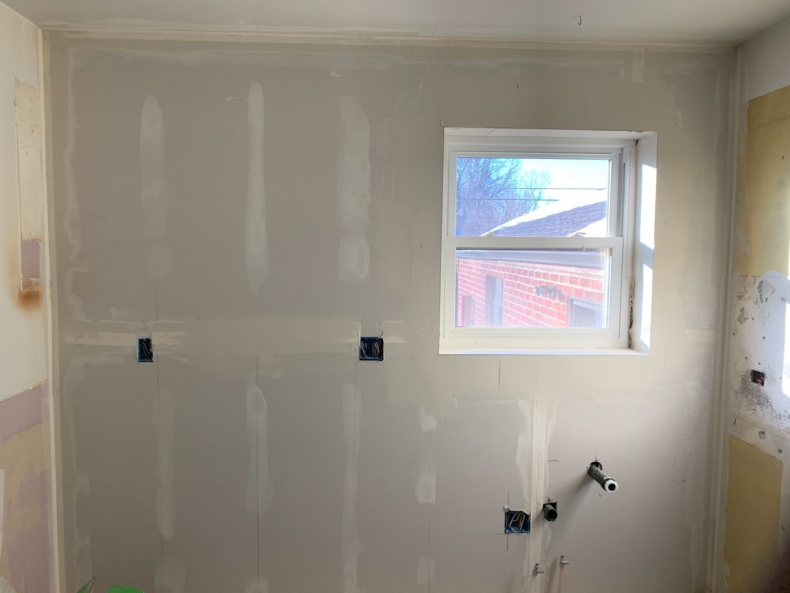 Interior wall with newly installed drywall, window, and electrical boxes.