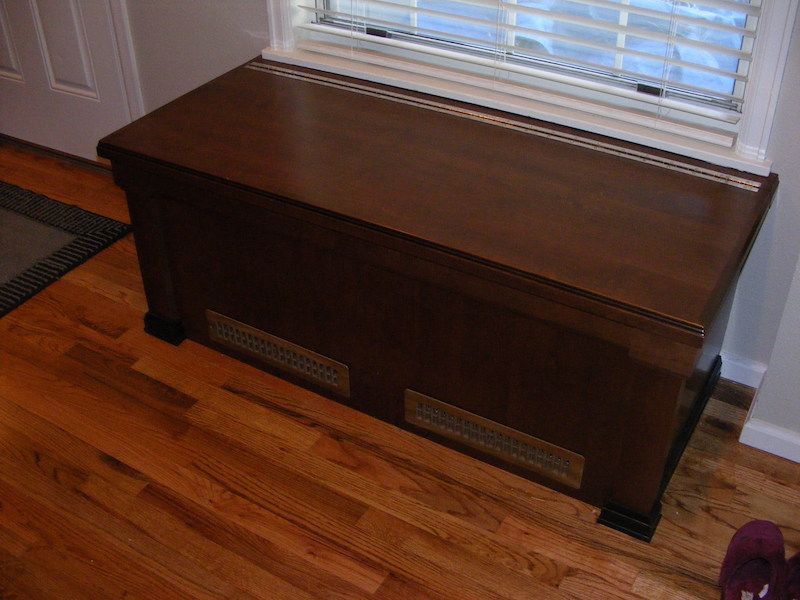 Wooden chest-like radiator cover beneath a window, on hardwood floor.