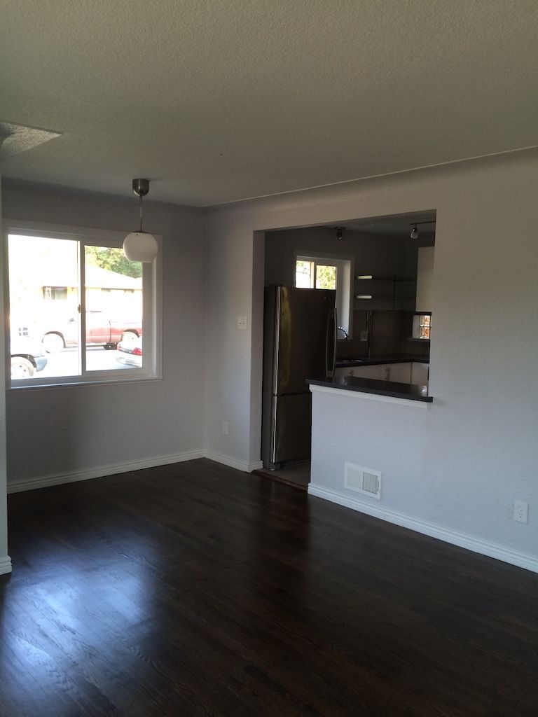 Interior of a room with dark wood floors, light gray walls, and an opening to a kitchen.