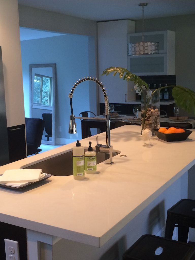 Modern kitchen island with sink, faucet, and soap bottles. White countertop, black stools.
