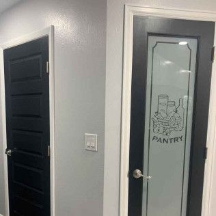 Two interior doors, one solid black, the other with frosted glass and pantry label. Gray wall.