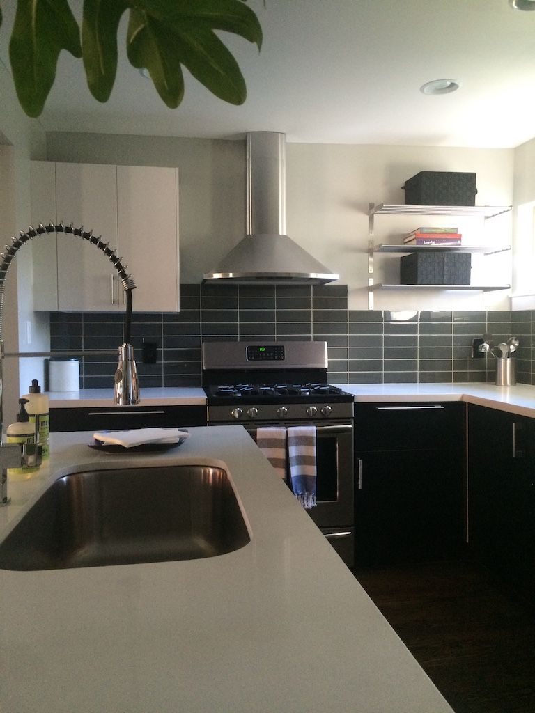Modern kitchen with white countertops, black cabinets, and a stainless steel range hood.