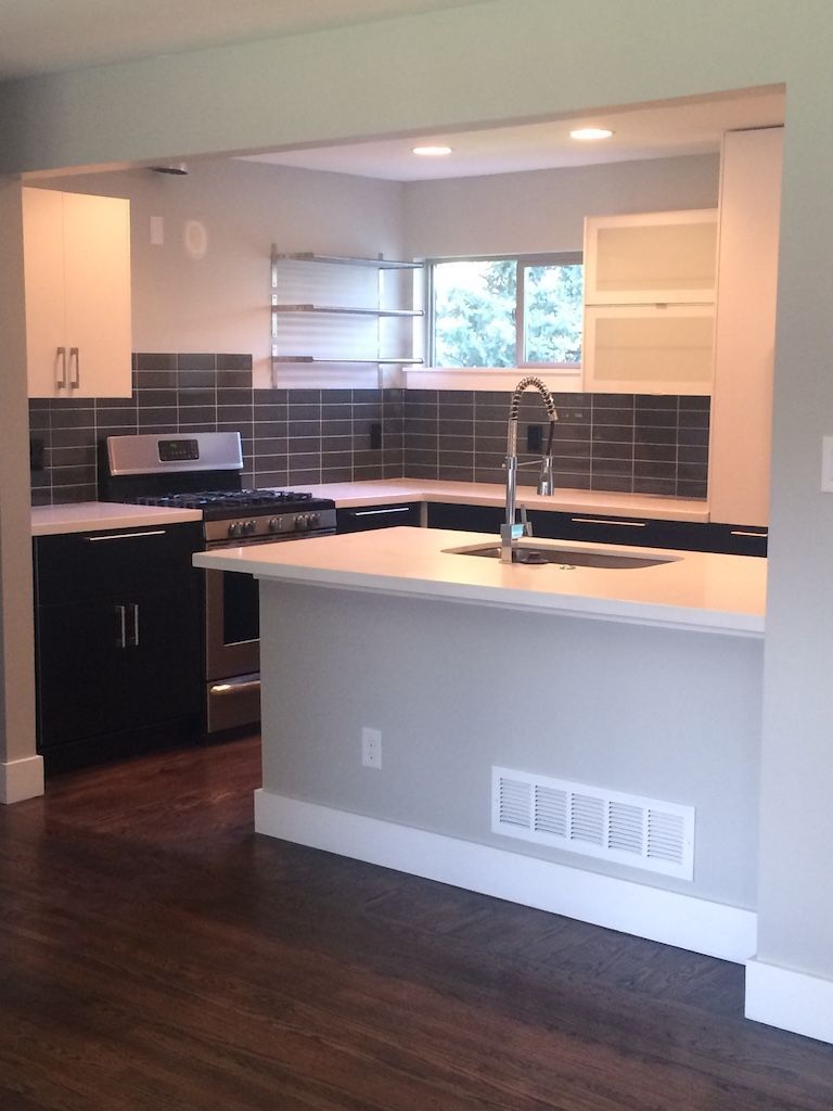 Modern kitchen with black and white cabinets, dark tile backsplash, and light gray walls.