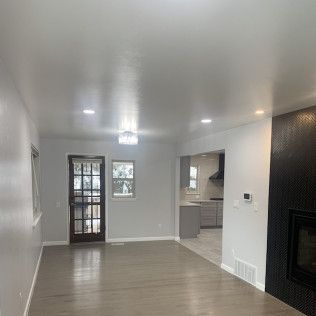 Bright living room with gray walls, light wood floor, and doorway to a kitchen.