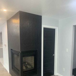 Black tiled fireplace with a black framed firebox, next to a black door and gray walls.