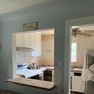 Kitchen pass-through during renovation. White cabinets, exposed wall, blue paint, open doorway, countertop.