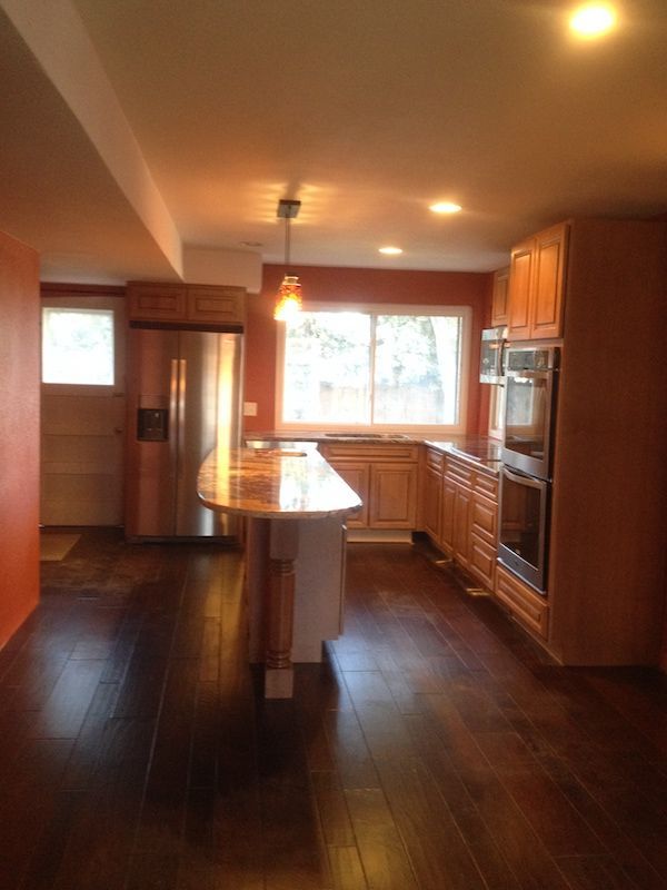 Kitchen with wood cabinets, island, stainless steel refrigerator, and dark wood floor.